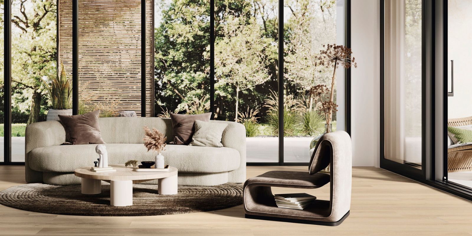 Modern living room with curved beige sofa, sculptural lounge chair, round coffee table, and floor-to-ceiling windows overlooking a green garden.