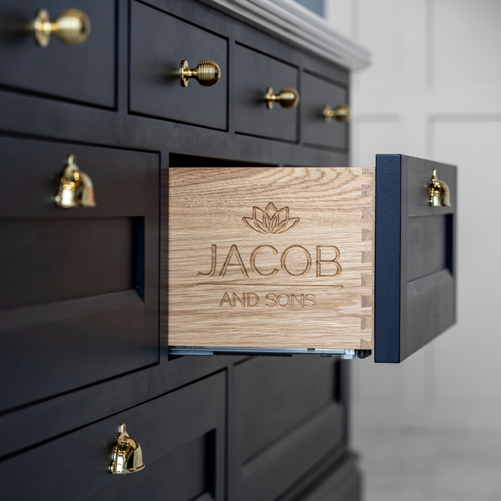 Wooden box with 'Jacob and Sons' engraving on a dark wooden cabinet with gold handles.
