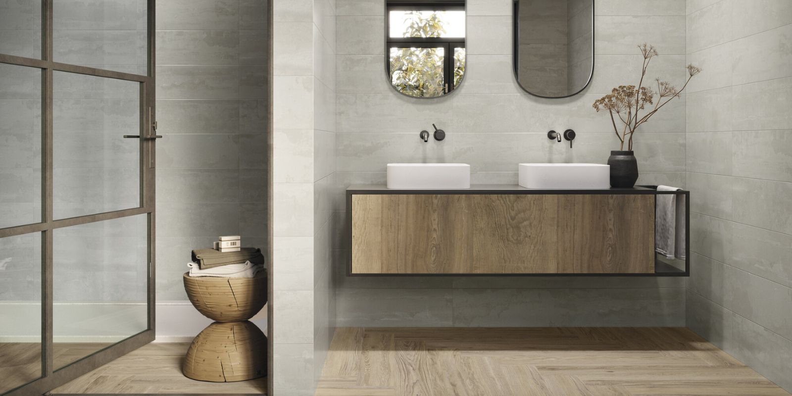 Modern bathroom with two sinks on a floating vanity, dual mirrors, dark beige herringbone floor tiles, and light grey wall tiles.