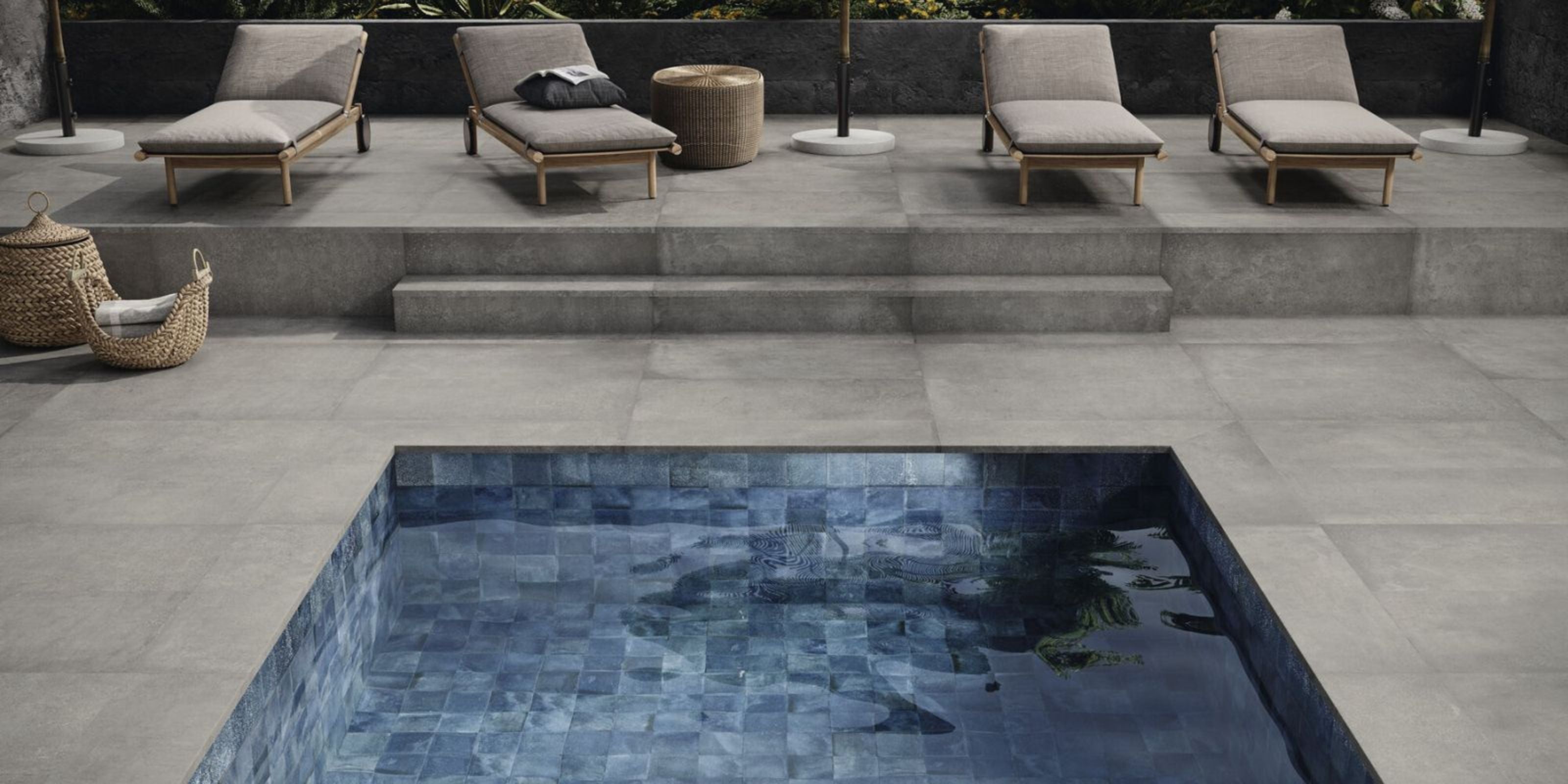 grey cement effect large format floor tiles with grey loungers and blue pool.