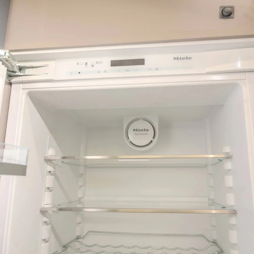 Miele refrigerator with open door showing interior shelves and control panel.