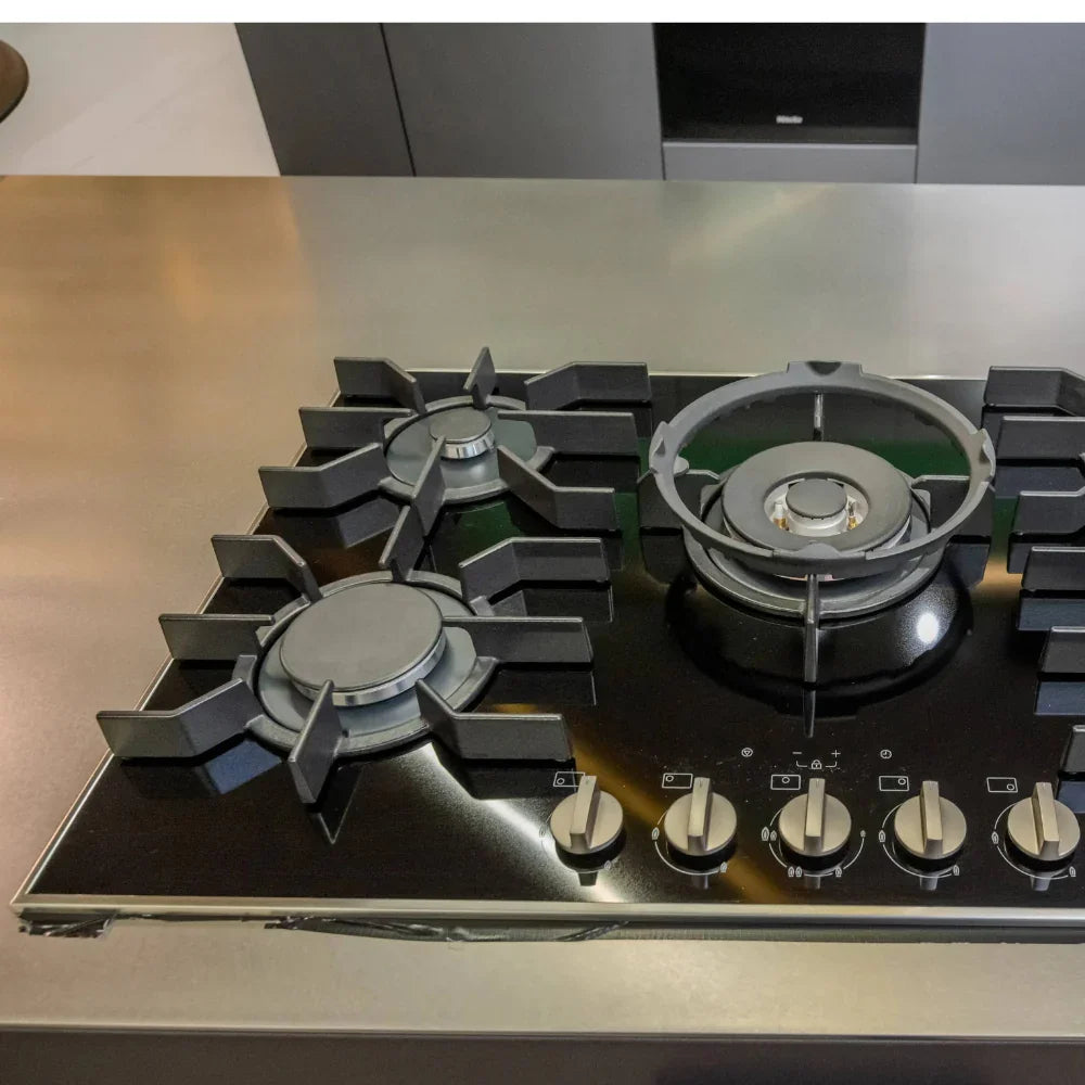 Stainless steel gas stove with multiple burners on a kitchen counter.