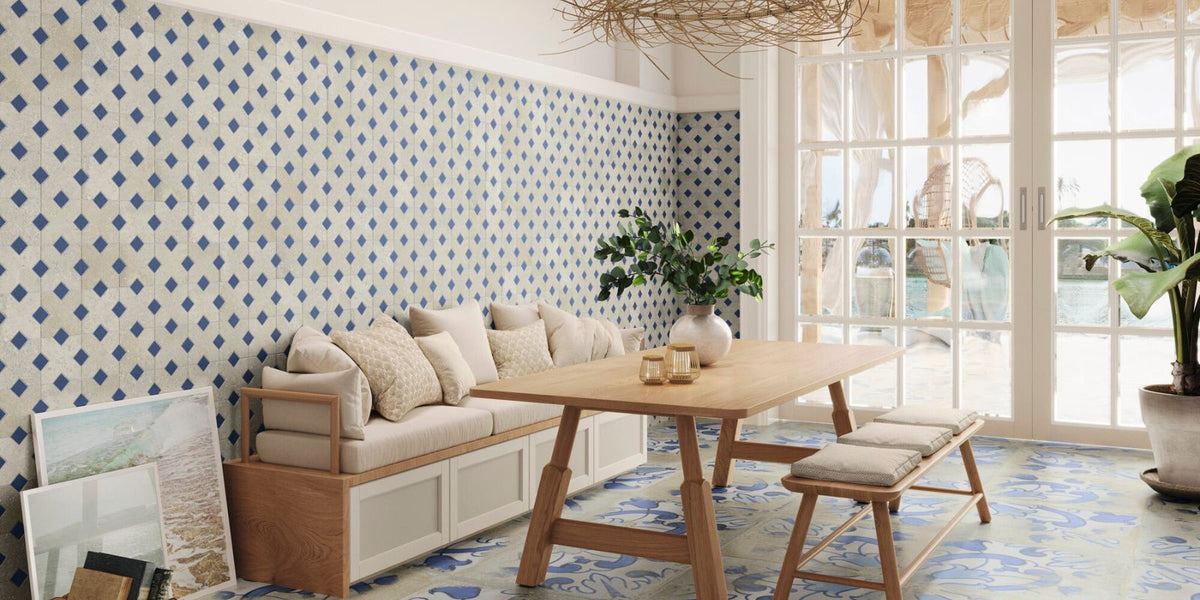 Bright dining area with patterned blue-and-white tiled walls, wooden table and bench, soft cushioned seating, and large windows overlooking a pool.