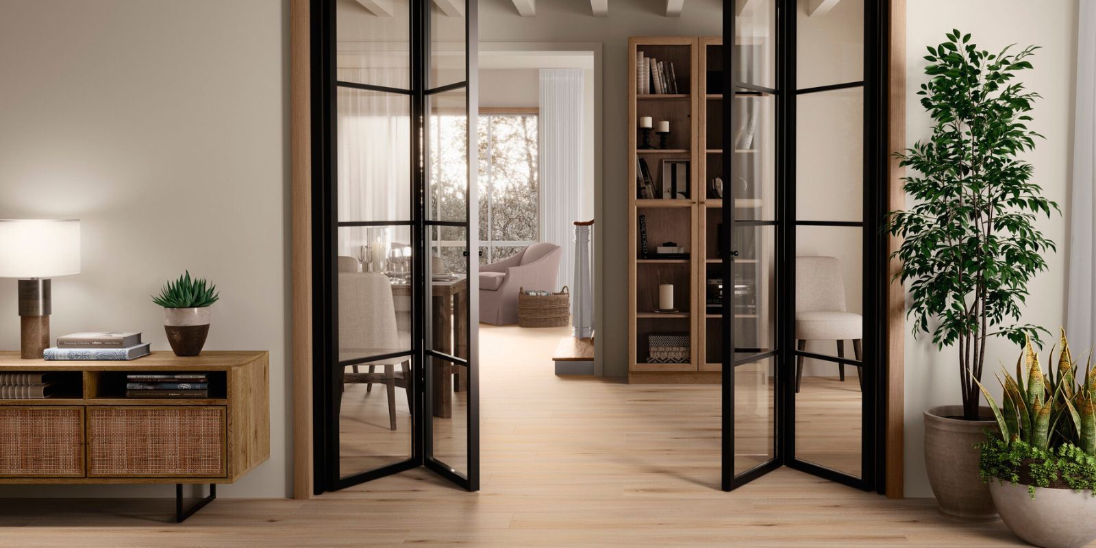 Bright and airy living space featuring light wood flooring, black-framed glass doors, indoor plants, and natural wood furniture with a cosy reading nook beyond.