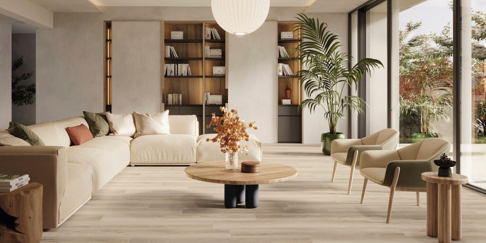 Bright modern living room with beige sofa, round wooden coffee table, indoor plants, and large floor-to-ceiling windows.