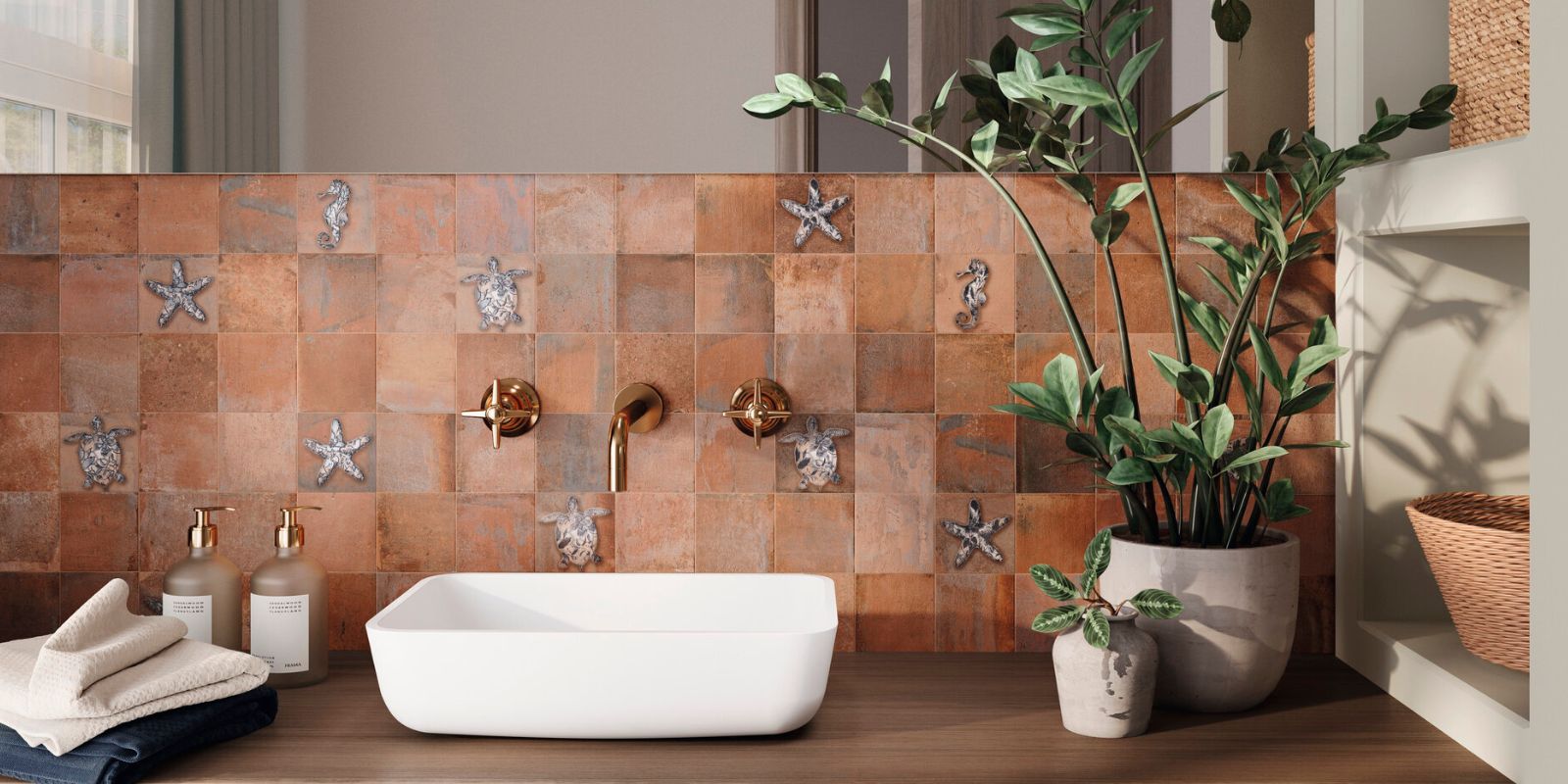 Bathroom sink area with terracotta tiles featuring sea motifs, a white basin, brass fixtures, and potted plants.