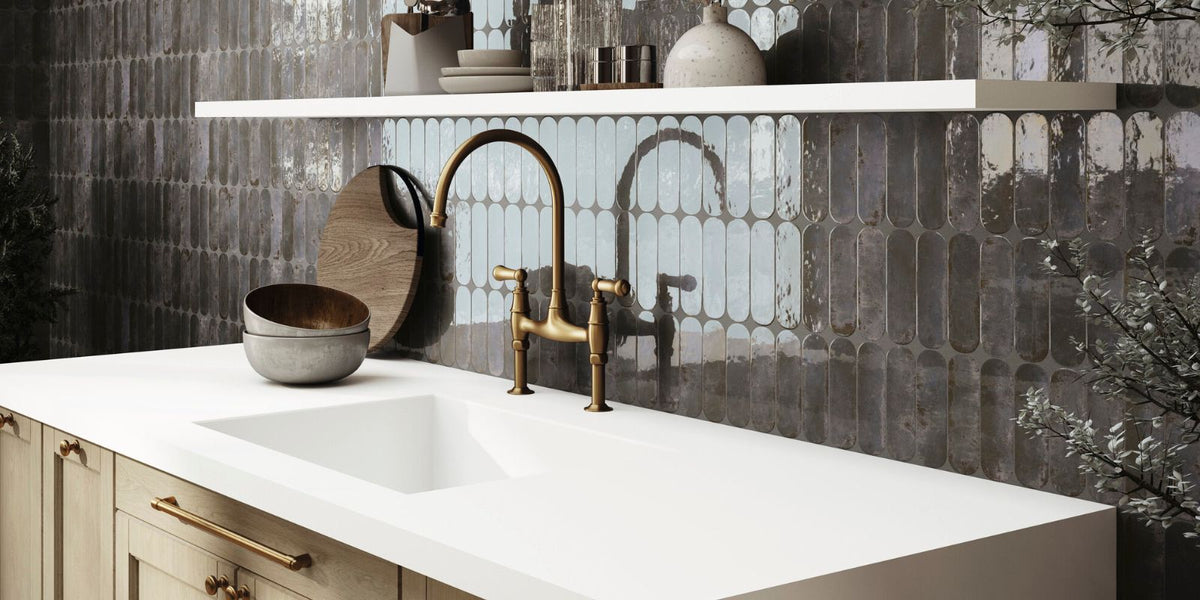  a stylish kitchen with a matte gold faucet, light wood cabinets, and glossy dark tiles with an elongated oval pattern. The contrast between the white countertop and the dark reflective backsplash creates a modern, luxurious feel.