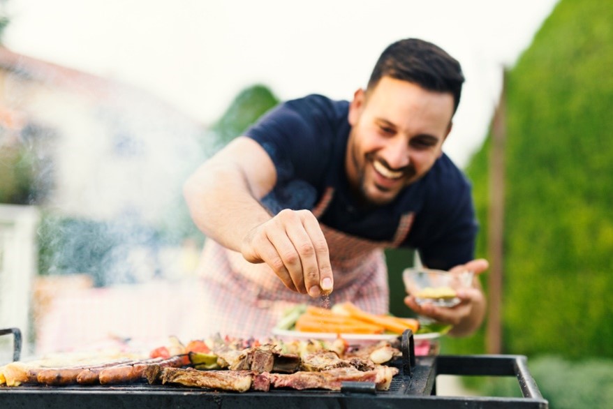 Man smiling while seasoning food on an outdoor BBQ