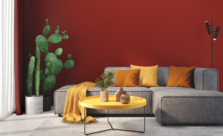 red living room wall with grey couch and yellow and orange cushions